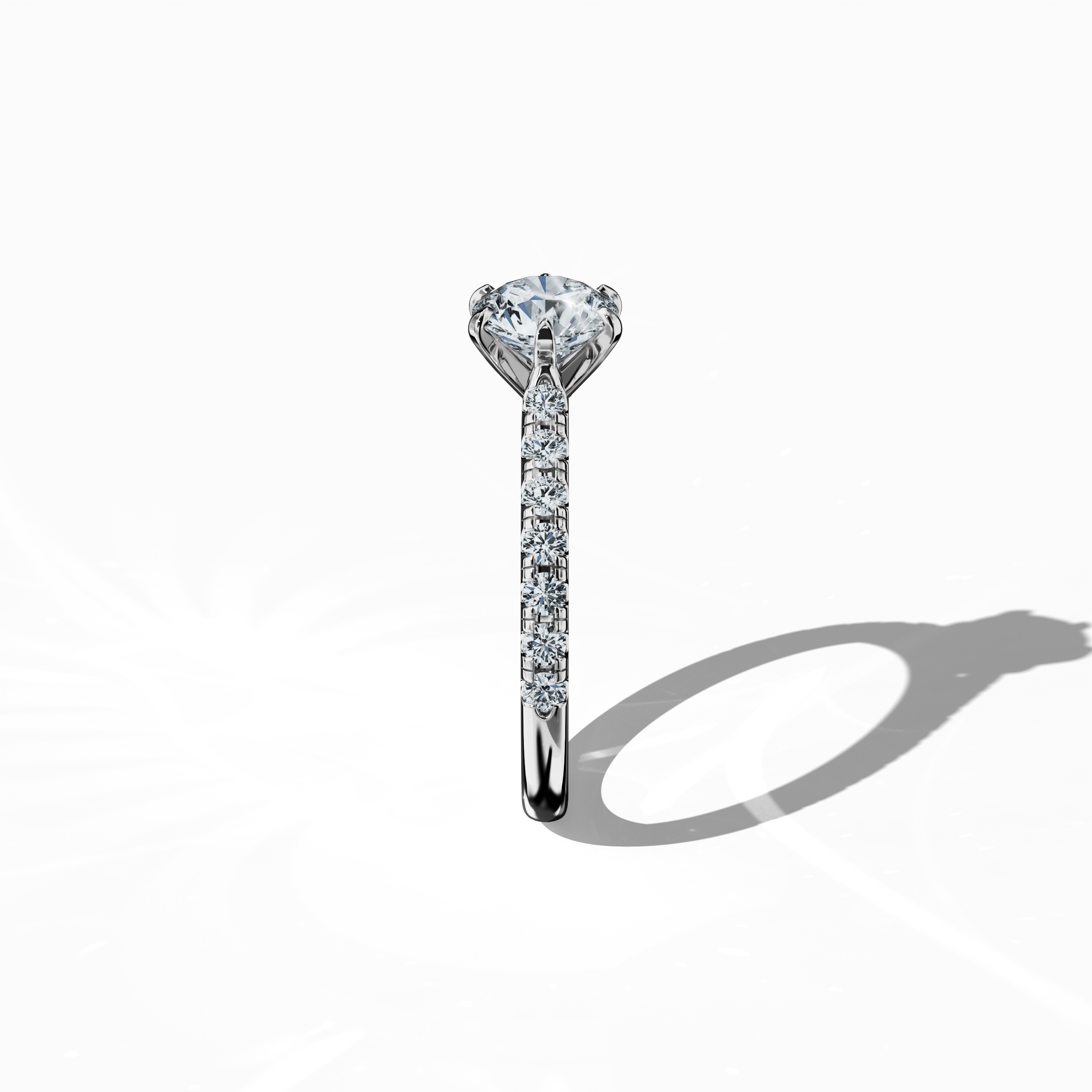 Side view of a white gold solitaire paved ring, highlighting a brilliant 1 ct center/centre diamond and 0.21 ct side diamonds along a slim band set in a refined four nail prong design. This perspective accentuates the ring’s elegant profile and minimalist design, making it an exquisite engagement ring, wedding band, or fine jewelry/fine jewellery accessory. Keywords: white gold, paved ring, diamond slim band, luxury, 1.21 ct, elegant design.