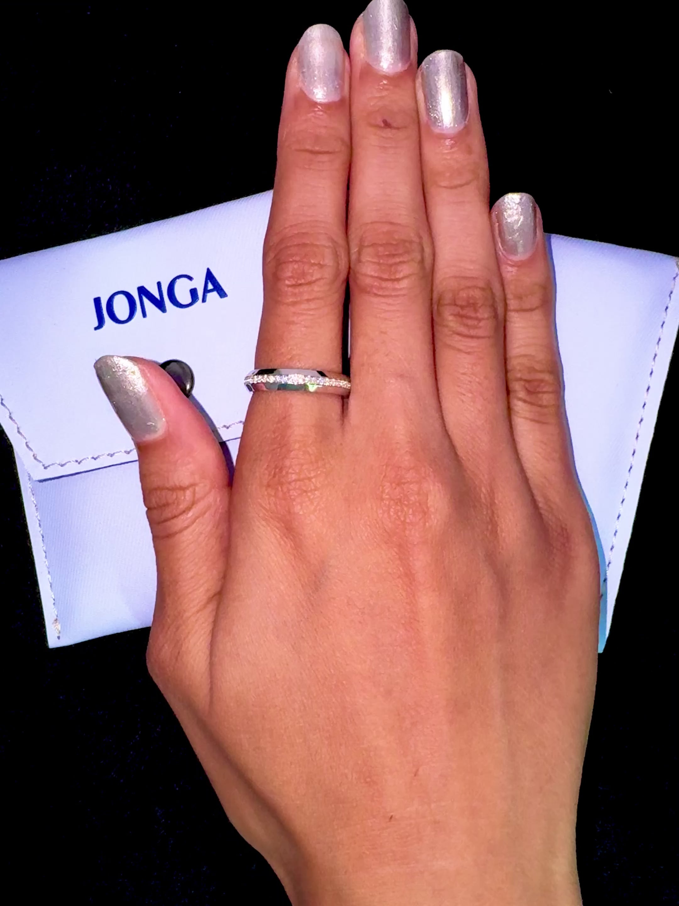 Elegant depiction of a 0.85 carat white gold paved band adorning a finger in a lifestyle “ring on her” shot. The ring spotlights a dazzling central design using pavé, full pave, scattered pave, and cluster pave techniques in luminous white gold—referred to as “opaline” or “milky gold.” Its glossy finish and refined detailing evoke a blend of contemporary allure and classic sophistication. Keywords: graceful, chic, luxurious, elegant, refined artistry.